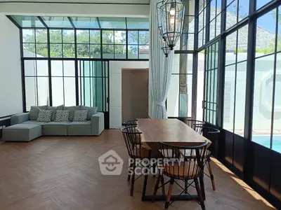 Modern living room with large windows and pool view, featuring stylish dining area and cozy sofa.