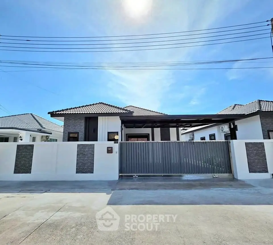 Modern single-story house with gated entrance and sleek design under a clear blue sky.