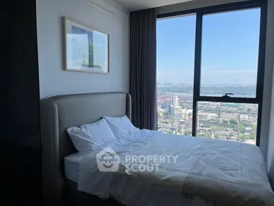Cozy bedroom with stunning city view from large window, perfect for urban living.