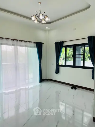 Spacious empty room with elegant chandelier and large windows offering natural light.