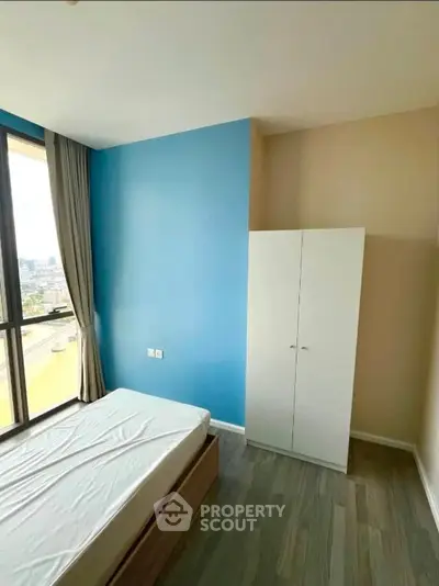 Bright bedroom with large window and modern wardrobe, offering city views and natural light.