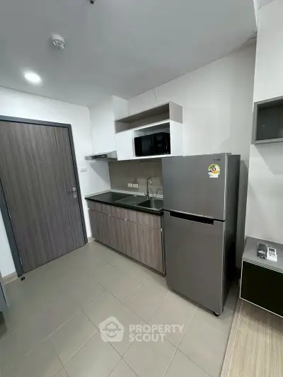 Modern kitchen with sleek cabinetry, stainless steel fridge, and microwave in a compact layout.
