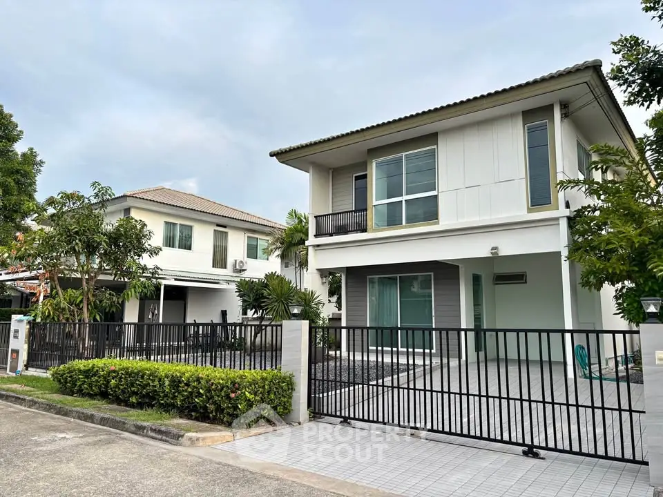 Modern two-story house with gated driveway and lush greenery in a serene neighborhood.