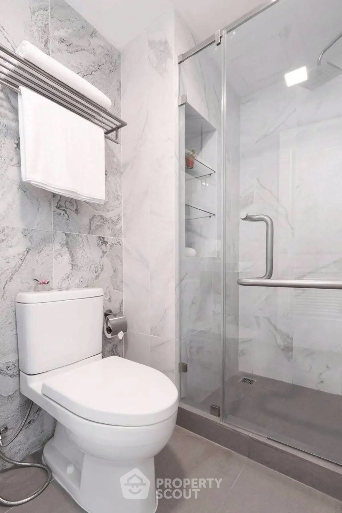 Modern bathroom with glass shower and marble walls, featuring sleek fixtures.