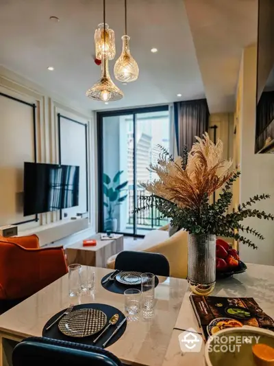 Chic modern living room with elegant pendant lights, plush seating, and a welcoming dining area, leading to a sunlit balcony.