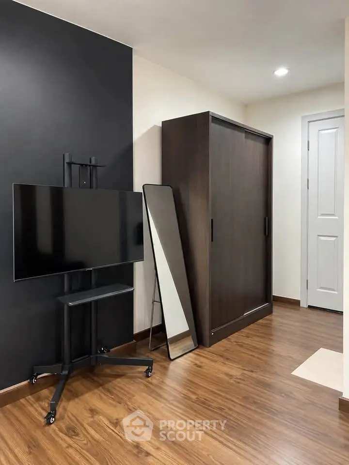 Modern interior with sleek TV stand, full-length mirror, and dark wardrobe on wooden flooring.
