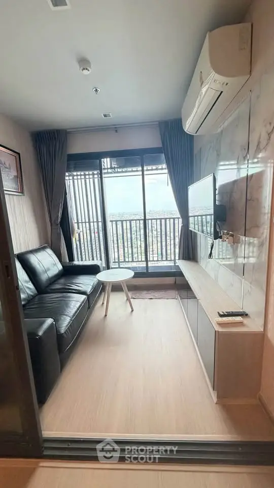 Modern living room with balcony view, sleek black sofa, and wall-mounted TV in a stylish apartment.