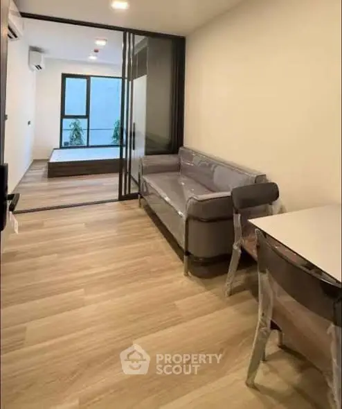 Modern apartment interior with open living room and bedroom layout, featuring sleek furniture and wooden flooring.
