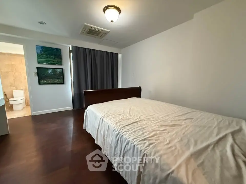 Spacious bedroom with elegant wooden flooring and cozy bed, adjacent to a modern bathroom.