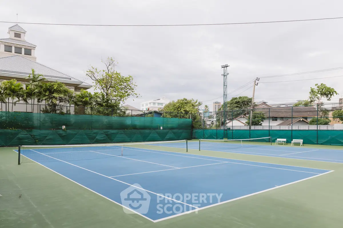 Spacious outdoor tennis court in a residential complex with lush greenery.
