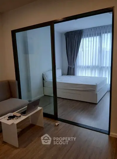 Modern apartment with glass partition separating living area and bedroom, featuring sleek furniture.