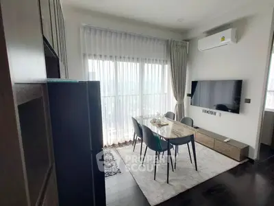 Modern living room with dining table, large TV, and floor-to-ceiling windows.