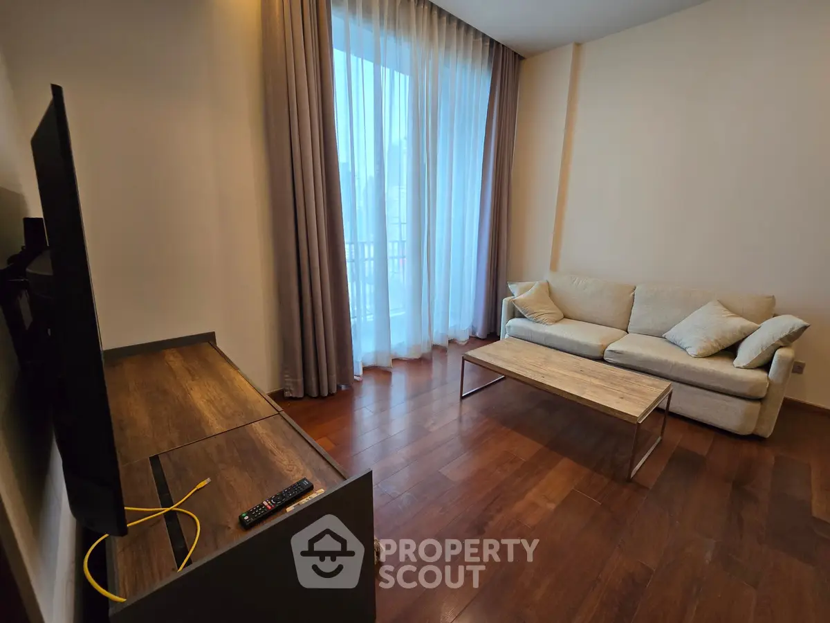 Modern living room with cozy sofa and large window, featuring wooden flooring and stylish decor.