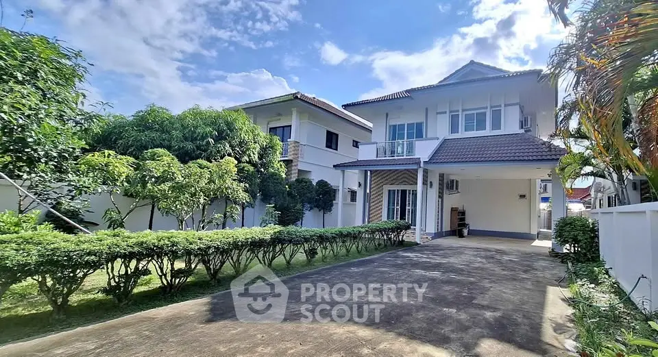 Charming two-story house with lush garden and spacious driveway under a clear blue sky.