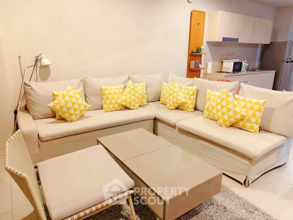 Modern living room with stylish beige sofa and yellow accent pillows, open kitchen layout, and cozy decor.