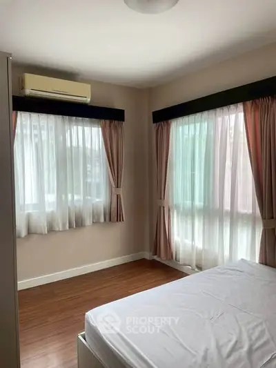Bright bedroom with large windows and wooden flooring, featuring elegant curtains and air conditioning.