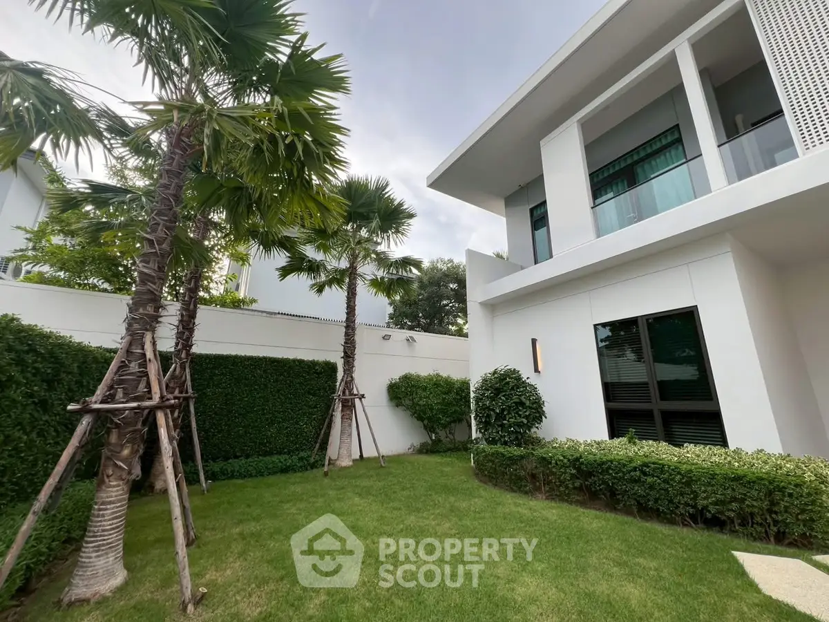 Modern white building with lush green garden and palm trees