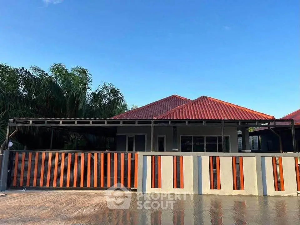 Charming single-story house with red roof and modern fence under clear blue sky.