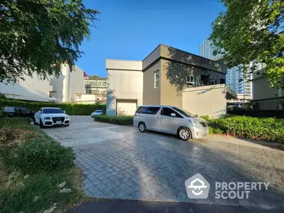 Modern urban home with spacious driveway nestled between lush greenery and high-rise buildings, offering a unique blend of privacy and city living.