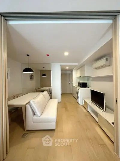 Modern open-plan living room with dining area and kitchen, featuring sleek furniture and wooden flooring.