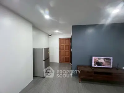 Modern living room with sleek design, featuring a wooden door, TV unit, and stainless steel refrigerator.