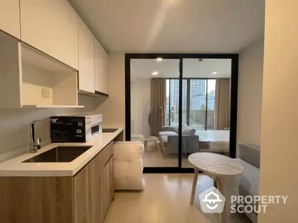 Modern apartment showcasing a sleek kitchen with built-in appliances leading to a cozy living area with natural light and balcony access, perfect for urban living.