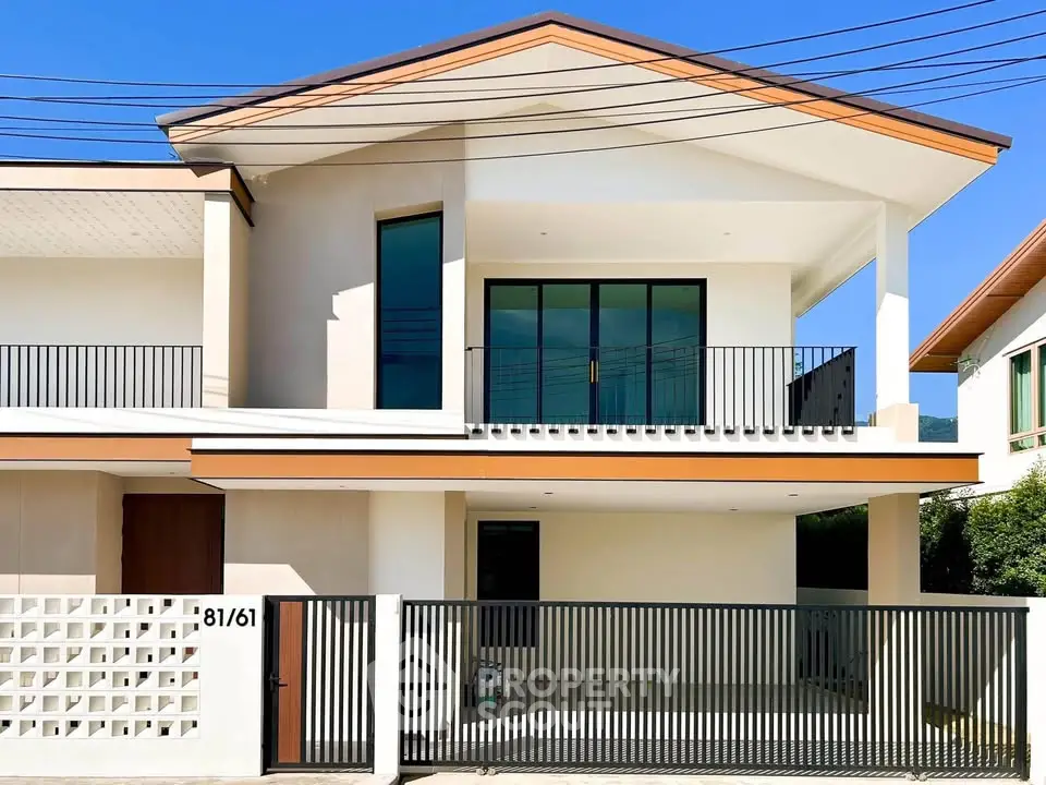 Modern two-story house with sleek design and spacious balcony, featuring a gated entrance and large windows.