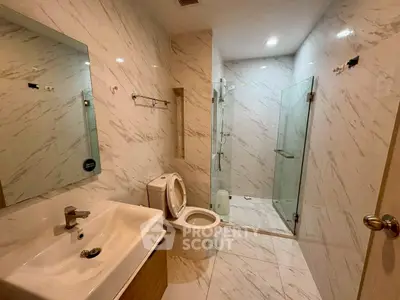 Modern bathroom with marble tiles, glass shower, and sleek fixtures.