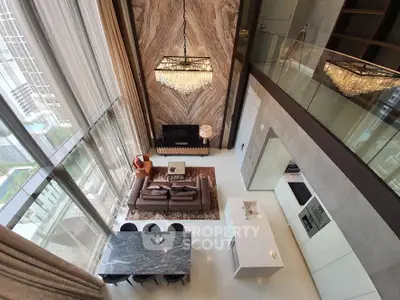 Luxurious double-height living room with marble floors, modern furniture, and elegant chandeliers, boasting natural light and sophisticated ambiance.
