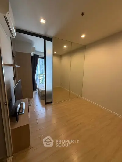 Modern living room with mirrored wall and wooden flooring, featuring a sleek TV setup and natural light.