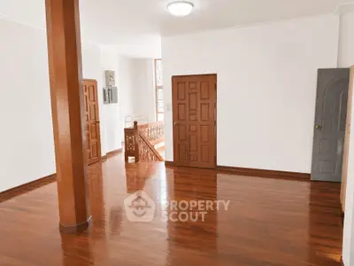 Spacious wooden-floored room with elegant staircase and natural light