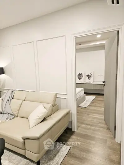 Modern living room with beige leather sofa and view into a stylish bedroom