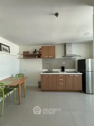 Modern kitchen with wooden cabinets, stainless steel fridge, and dining area in open layout apartment.