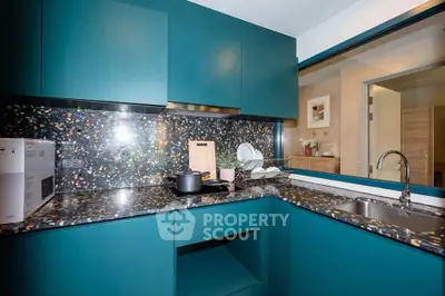 Modern kitchen with teal cabinets and terrazzo countertops, featuring sleek design and open layout.