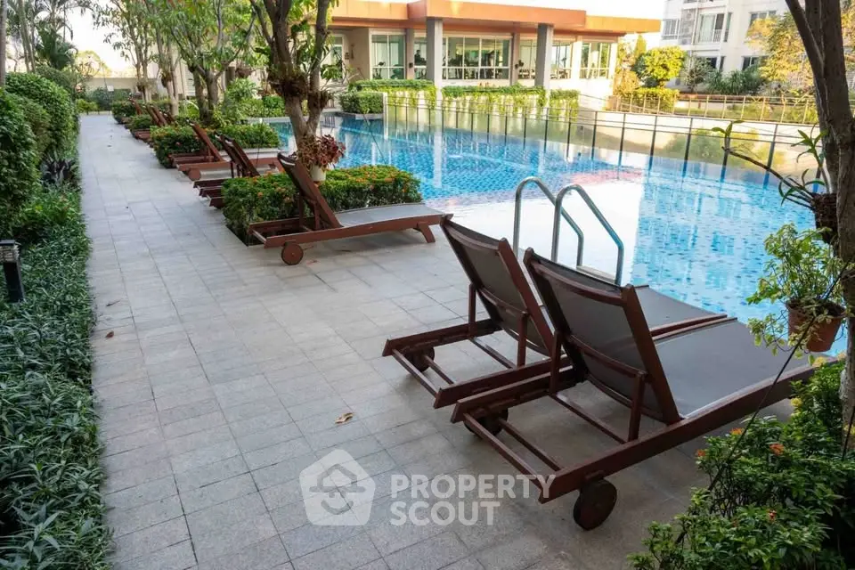 Luxurious poolside area with sun loungers and lush greenery in modern residential complex.