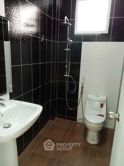 Modern bathroom with sleek black and white tiles, featuring a shower and toilet.