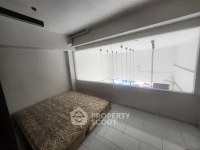 Compact bedroom with large window and minimalist design, featuring a simple mattress on tiled flooring.
