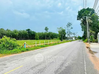 Scenic road view with lush greenery and open land, ideal for real estate development.