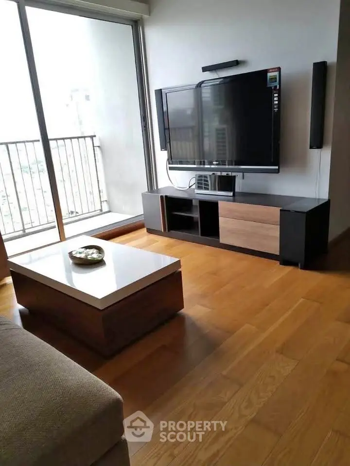 Modern living room with sleek TV setup and wooden flooring, featuring a balcony view.