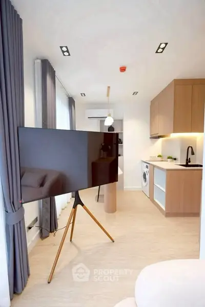 Modern living room with sleek TV, open kitchen, and washing machine in stylish apartment.