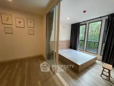 Modern bedroom with large windows and wooden flooring, offering a serene garden view.