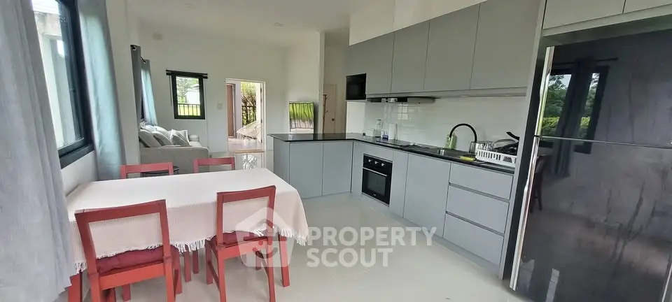 Modern open-layout kitchen with dining area and living room, featuring sleek cabinetry and stainless steel appliances.