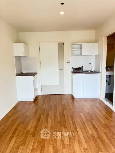 Modern compact kitchen with wooden flooring and sleek white cabinets in a cozy apartment.