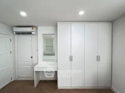 Modern white bedroom with built-in wardrobe and vanity, featuring sleek design and ample storage.