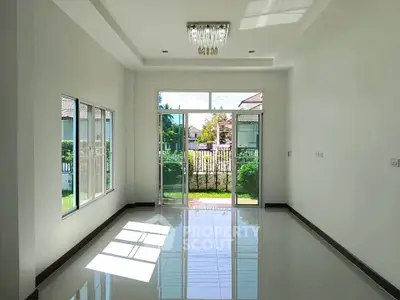 Spacious living room with large windows and garden view, featuring elegant chandelier and glossy tiled floor.