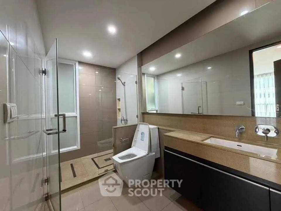 Spacious modern bathroom with glass shower and sleek vanity in luxury apartment.