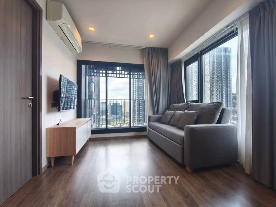 Modern living room with large windows and city view, featuring a comfortable sofa and sleek TV setup.