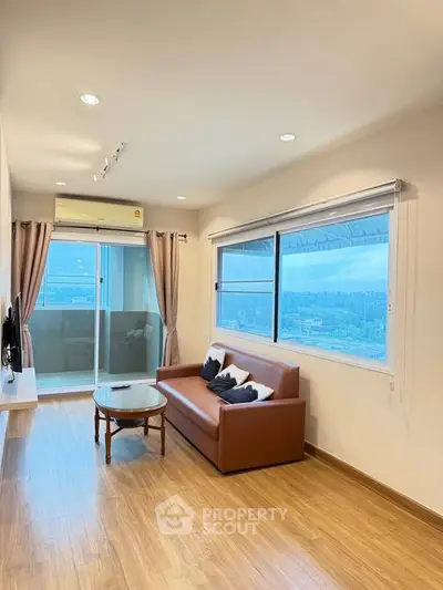 Modern living room with large windows and balcony view, featuring stylish furniture and wooden flooring.