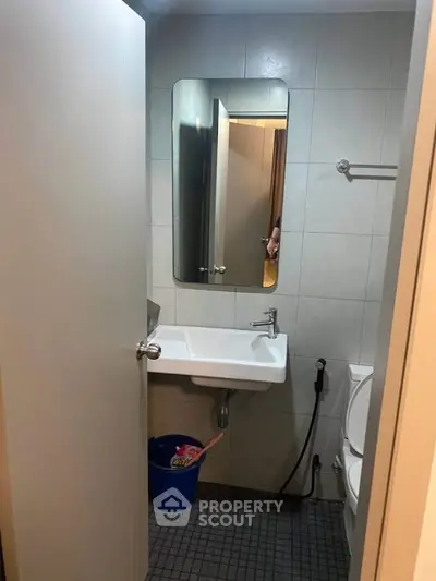 Compact bathroom with modern fixtures and tiled walls, featuring a sink, mirror, and toilet.