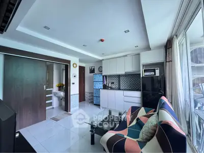 Modern living room with stylish furniture and open kitchen layout, featuring sleek cabinetry and large windows.